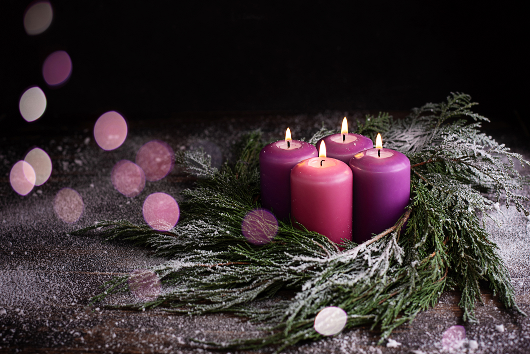 Wreath with four burning Advent candles on a dark wooden snowy background with festive lights