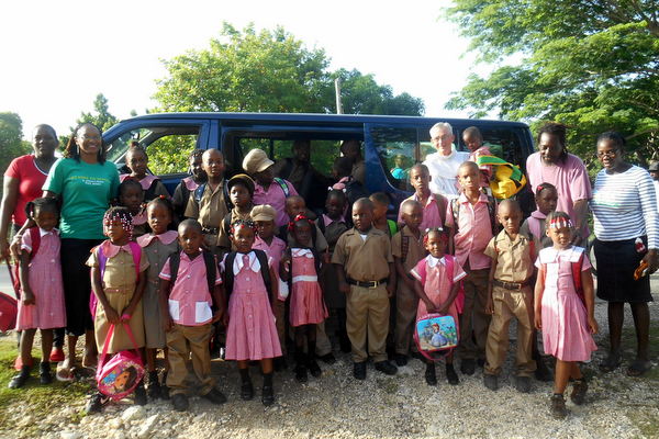 Students and parents stand in front of Josey the school van with Fr. Jim Bok, OFM, outside St. Anthony's Kitchen