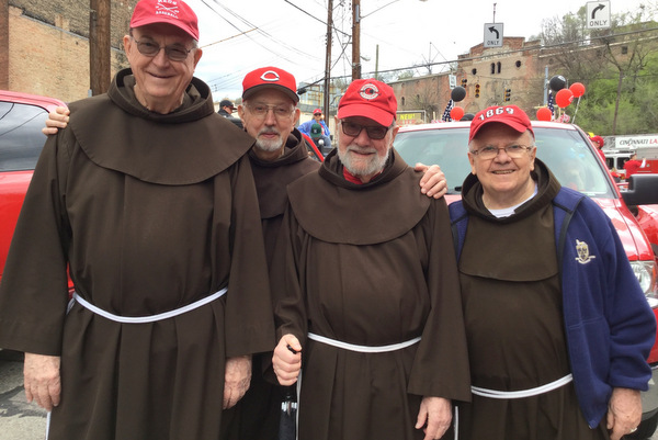 Friars John Bok, Dominic Lococo, Tom Speier, and Fred Link wearing habits and Reds hats