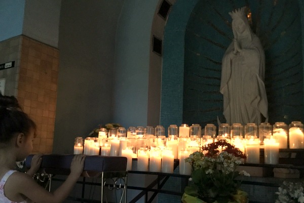 girl praying to OLO Guadalupe statue with candles