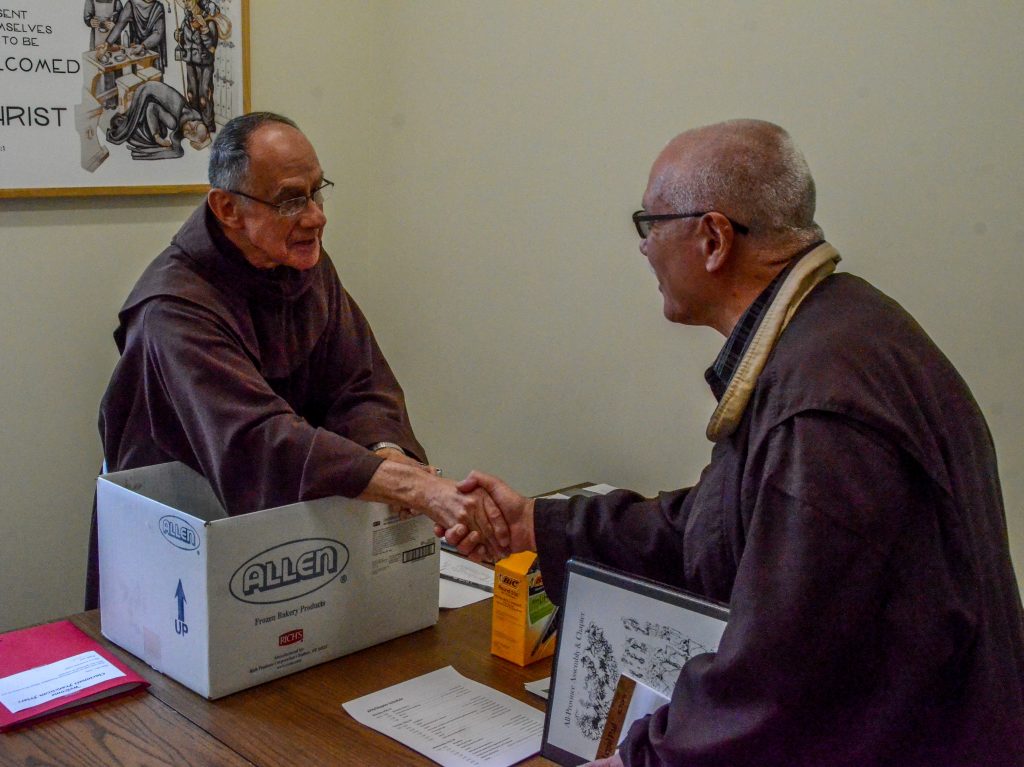 two friars shake hands